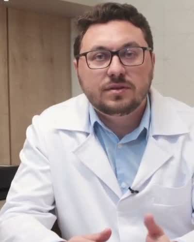 Dr. Tiago Martins, de jaleco branco, sentado à mesa do consultório.