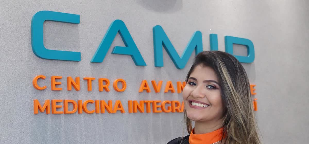 Recepção da clínica, com o letreiro CAMIP em letras de relevo na parede e uma recepcionista de uniforme ao lado.